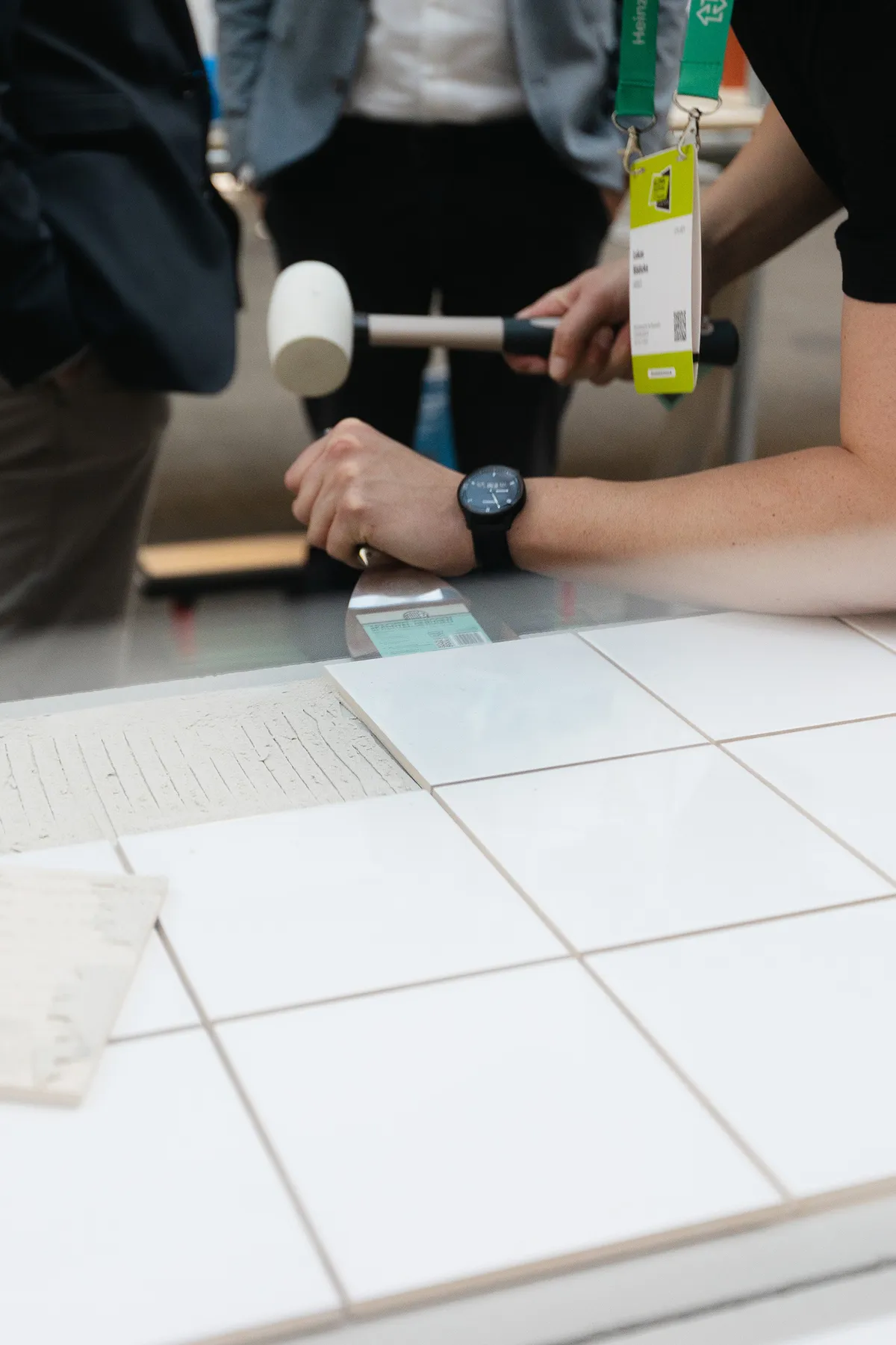 Person löst an der Rückbaustation des Ardex Messestands mit einem Gummihammer weiße Fliesen von einer Platte