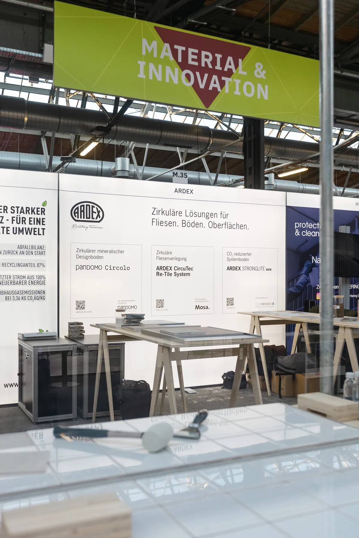 Ardex Messestand im Bereich »Material & Innovation« auf dem Heinze Klimafestival, Rückwand zu zirkulären Lösungen für Fliesen, Böden und Oberflächen, davor Arbeitstische