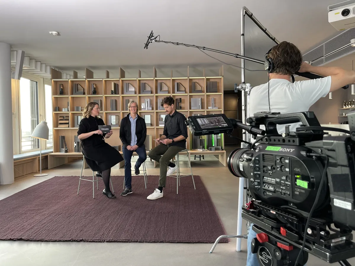 Dreh im Schüco Showroom Hamburg: Kamera und Tonangel vor einer Gesprächsrunde auf Barhockern vor einem Regal mit Profilmustern