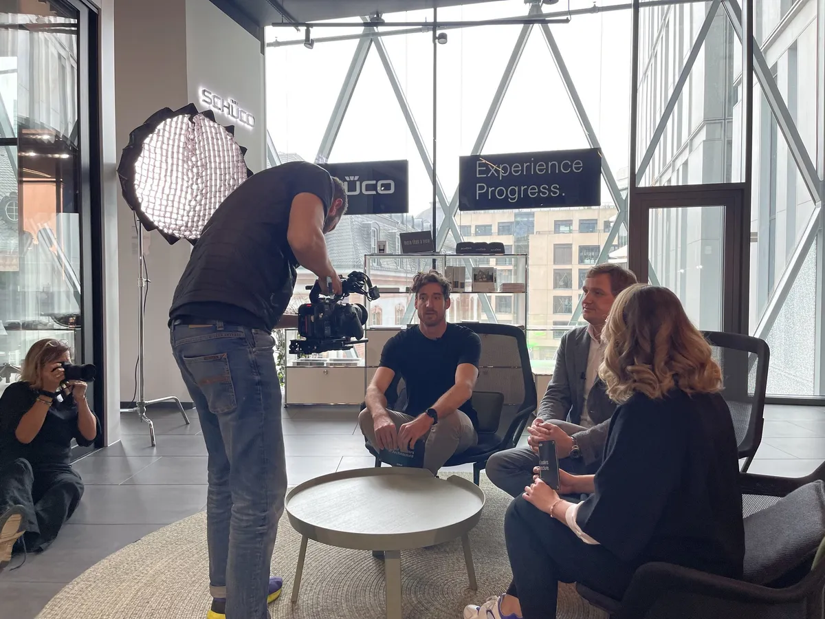 Kameramann und Fotografin filmen eine Gesprächsrunde im Schüco Showroom Frankfurt, daneben eine Softbox