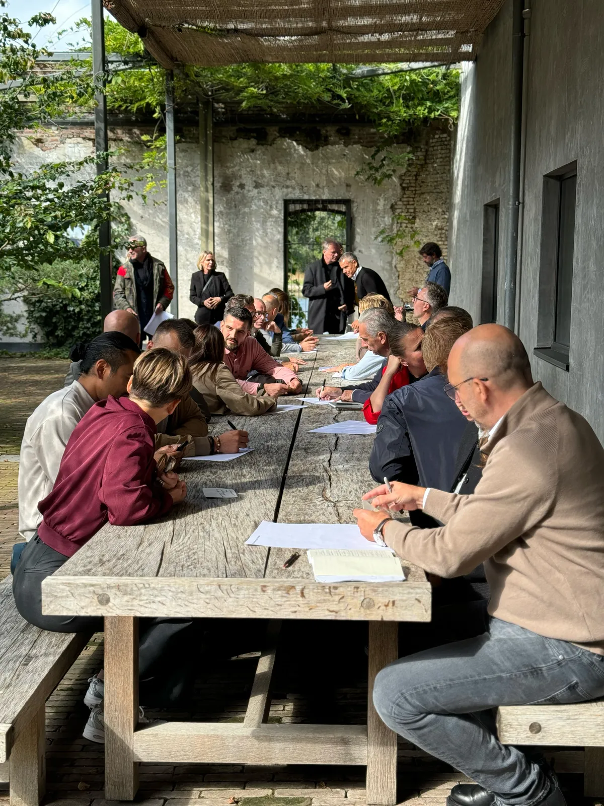 Teilnehmende des Ege Vertriebspartner:innen-Workshops arbeiten an einer langen Holztafel im Innenhof eines alten Backsteingebäudes in Antwerpen