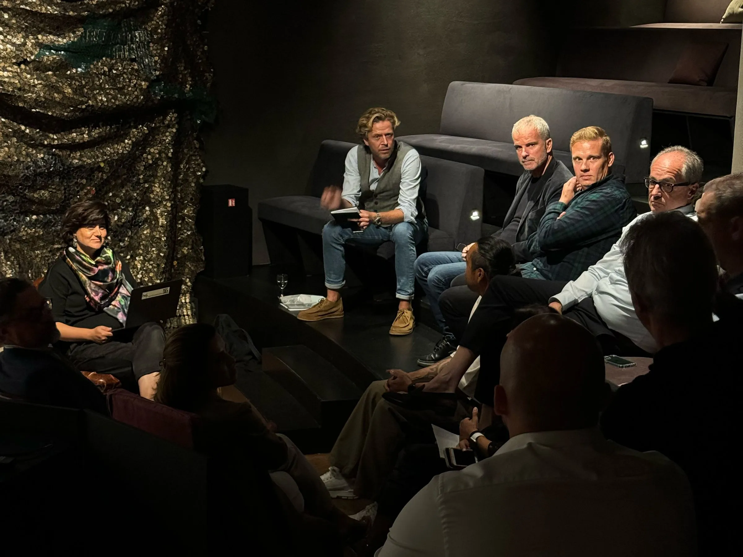 Gruppe von Teilnehmer:innen bei einer moderierten Diskussionsrunde in einem dunklen Veranstaltungsraum
