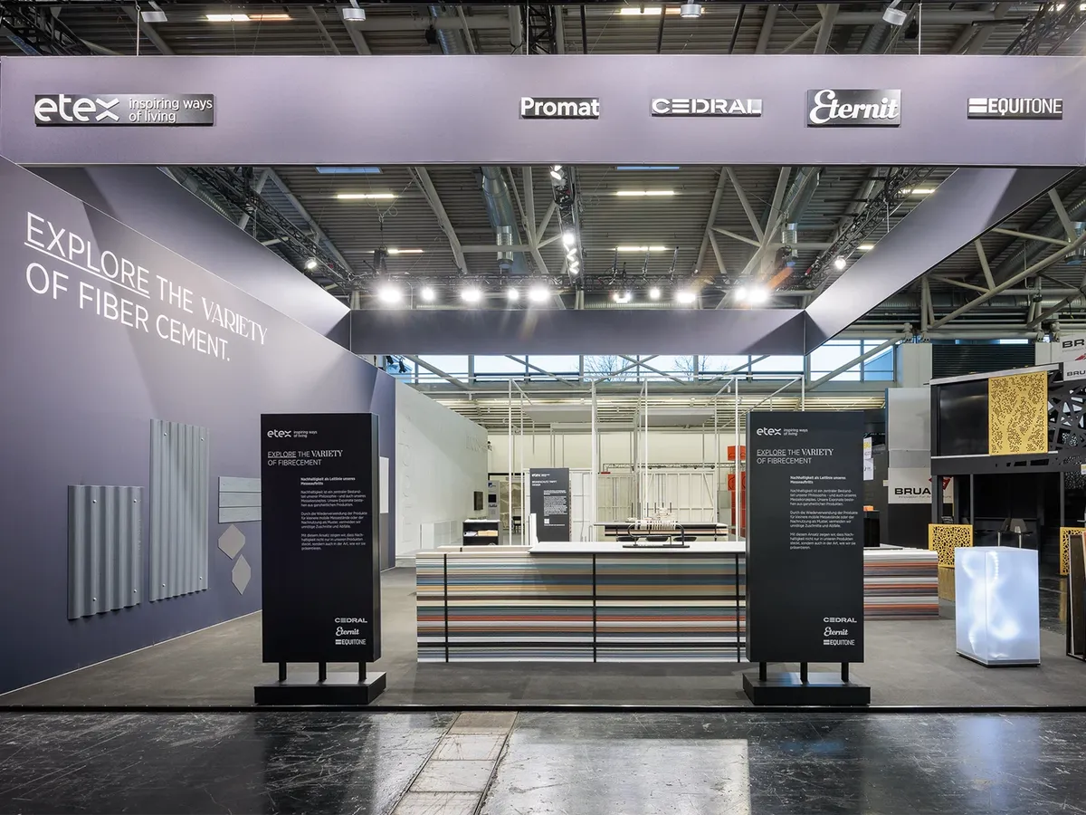 Etex Messestand auf der BAU 2025 mit den Marken Promat, Cedral, Eternit und Equitone, Wandschriftzug »Explore the variety of fiber cement«, Infostelen und einer Theke aus gestapelten Faserzementplatten
