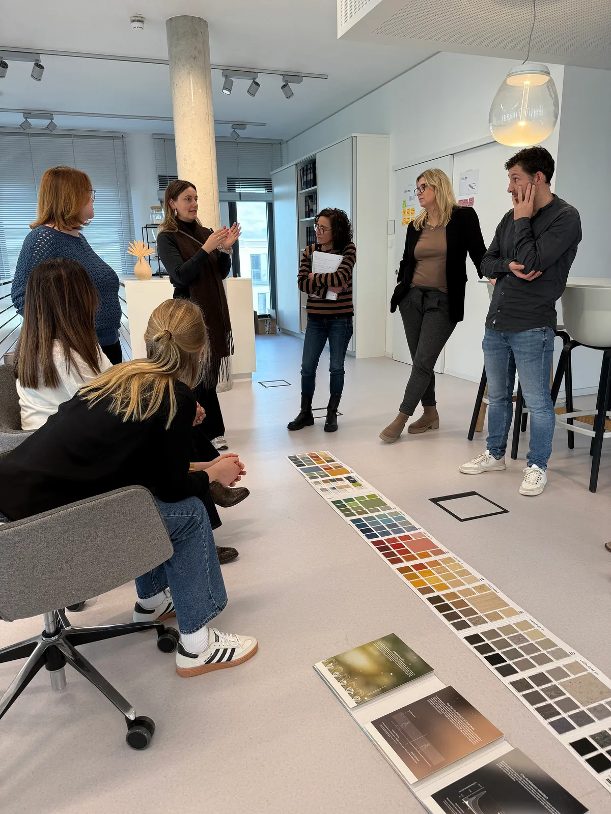 Workshop-Gruppe in einem hellen Raum, am Boden liegen Reihen von Tarkett-Farbmustern und Produktbroschüren