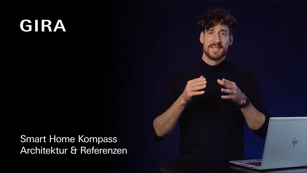 Standbild aus dem Gira-Video »Smart Home Kompass Architektur & Referenzen«: Person spricht vor dunklem Hintergrund neben einem Laptop