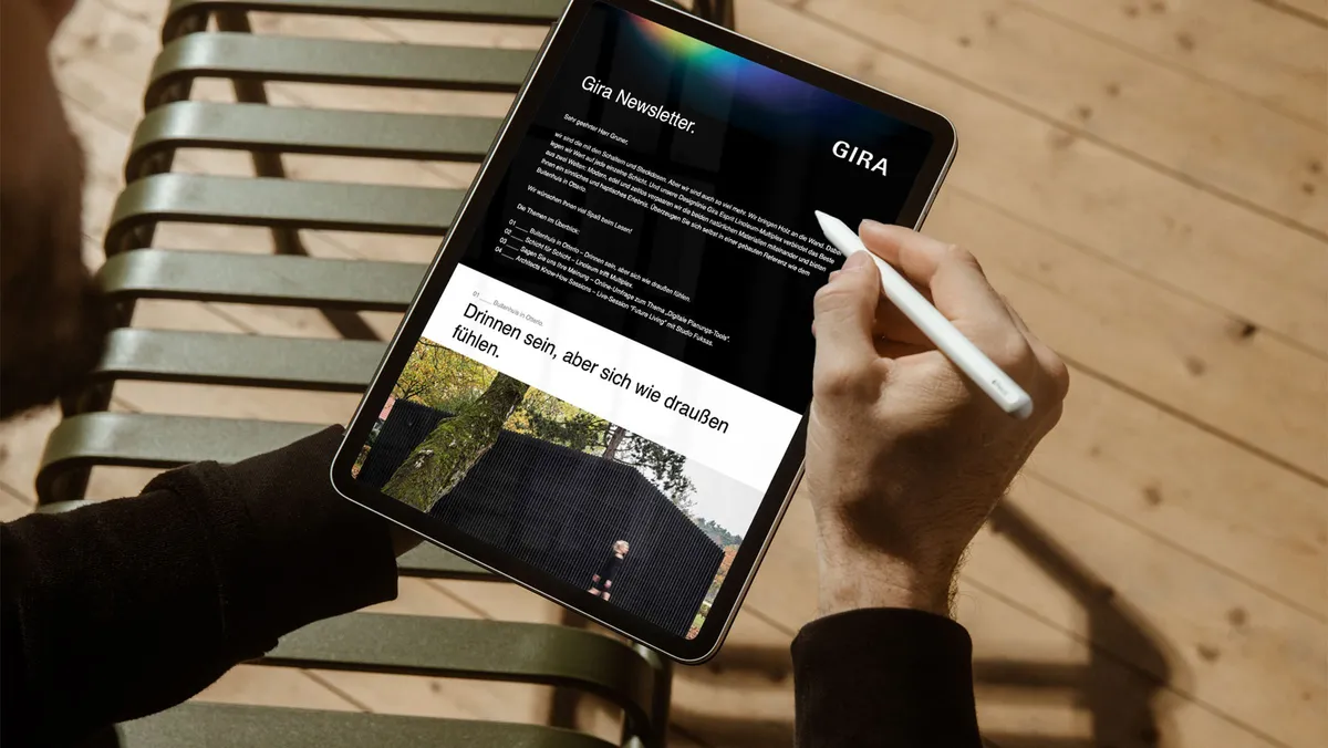 Person hält ein iPad mit Apple Pencil und liest den Gira Newsletter mit einem Architektur-Beitrag.