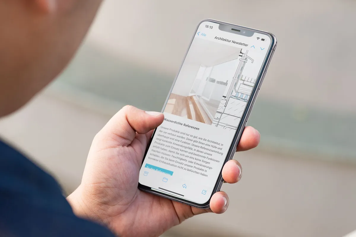 Hand hält ein Smartphone mit dem Gutjahr Architektur-Newsletter zum Thema wasserdichte Referenzen