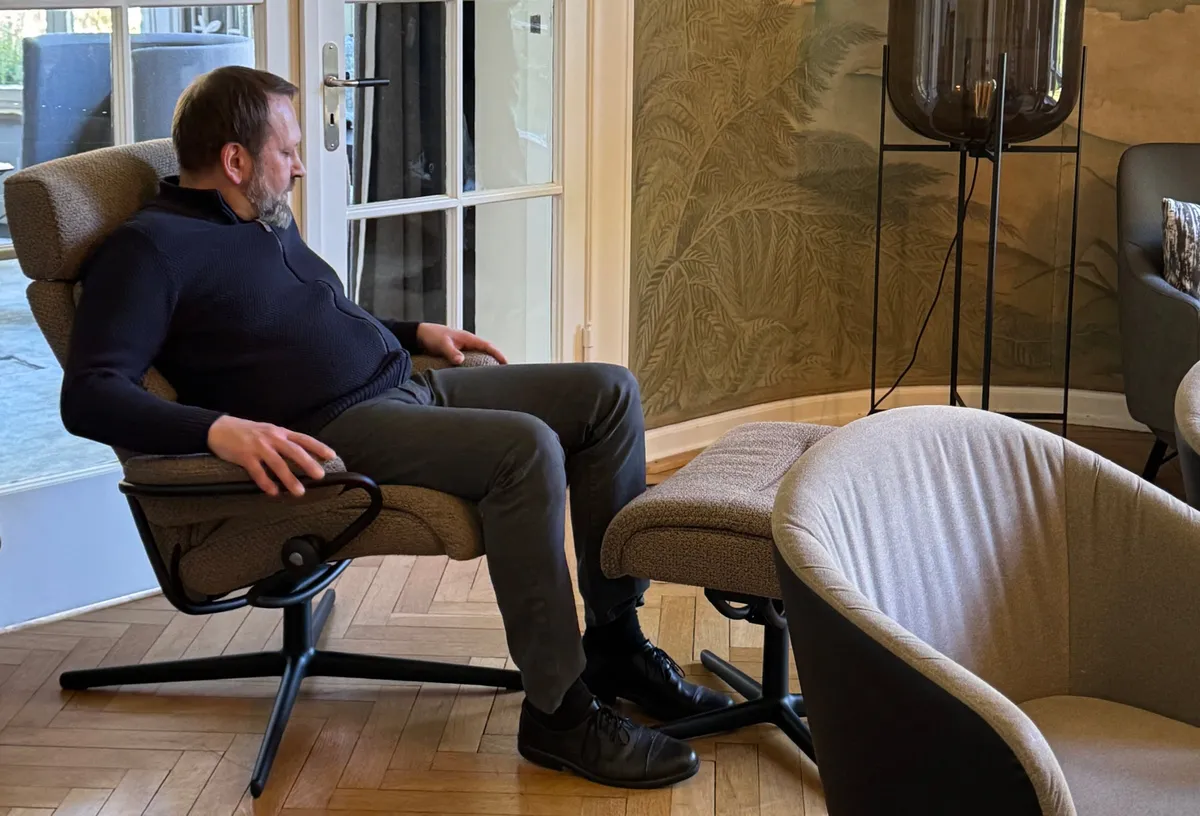 Ein Mann probiert einen Relaxsessel mit Hocker in einem Showroom mit großem Wandbild aus