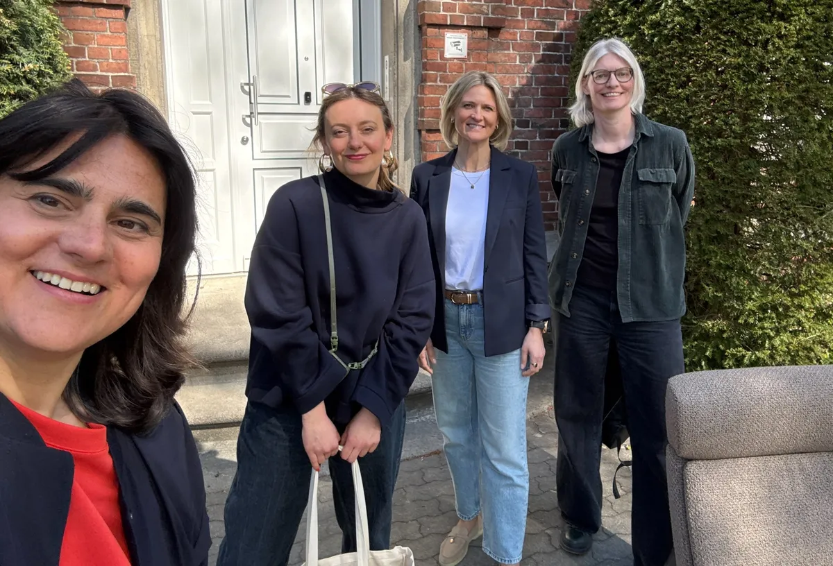 Selfie von vier Frauen vor dem Eingang eines Backsteinbaus, davor ein Stressless-Sessel