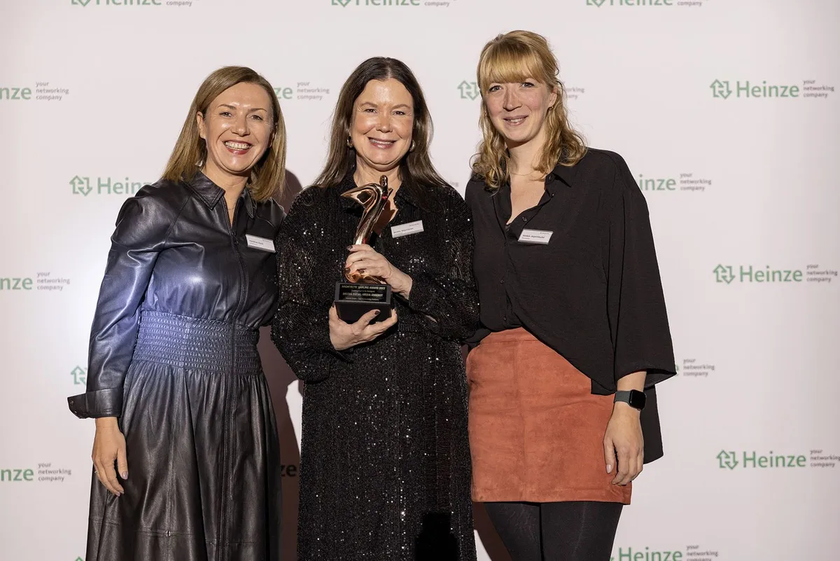 Drei Personen mit der Trophäe des Architects' Darling Award vor einer Heinze-Fotowand