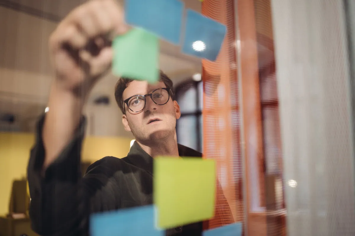 Workshop-Teilnehmer ordnet farbige Haftnotizen an einer Glaswand während des Nachhaltigkeits-Strategieworkshops bei TECE