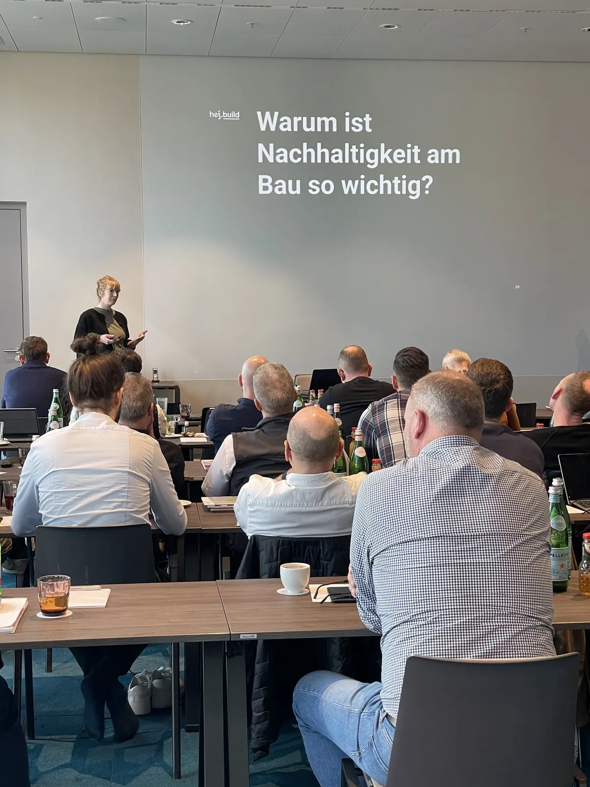 Saskja Jagenteufel vor der Folie »Warum ist Nachhaltigkeit am Bau so wichtig?« beim Live-Training, im Vordergrund das Vertriebsteam