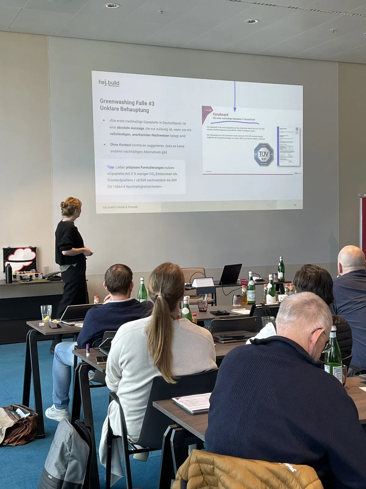 Folie »Greenwashing-Falle #3: Unklare Behauptung« beim Live-Training, im Vordergrund Teilnehmende an Tischen
