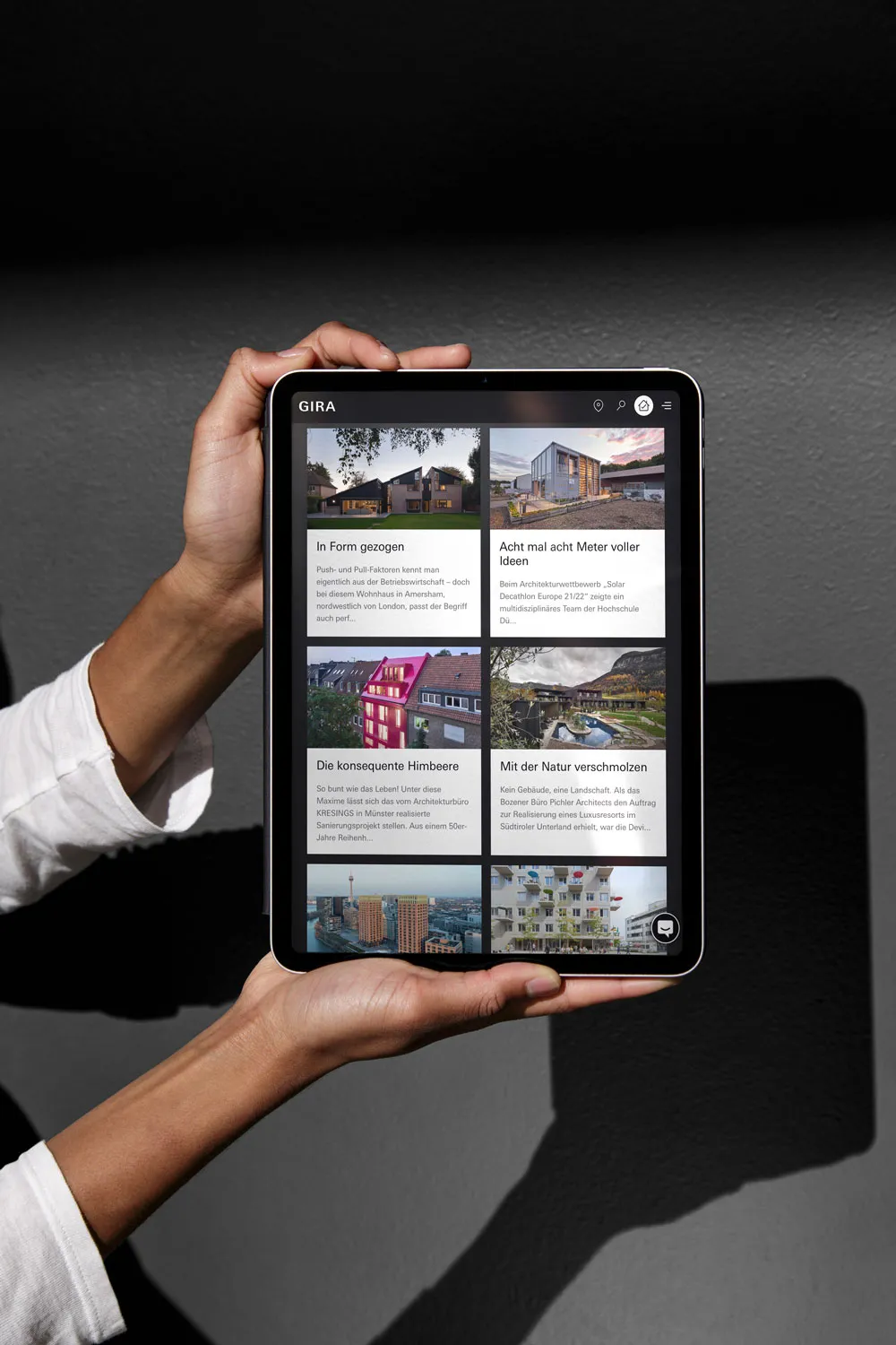 Hände halten ein Tablet mit der Übersicht der Gira-Referenzberichte vor grauem Hintergrund