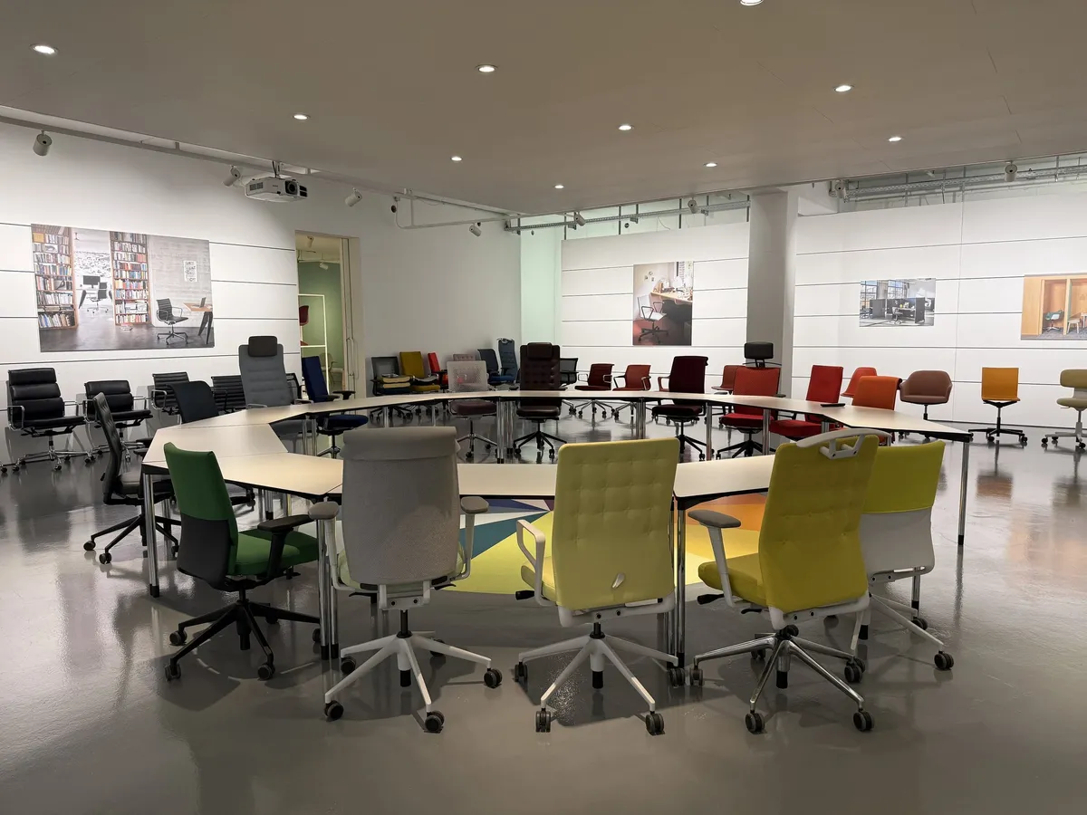 Kreis aus Bürostühlen in verschiedenen Farben um einen runden Tisch in einer hellen Ausstellungshalle