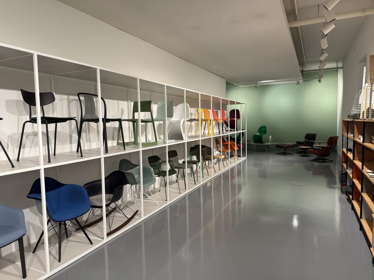 Weiße Regale mit Stühlen in Blau, Schwarz und Grün in einer Ausstellungshalle