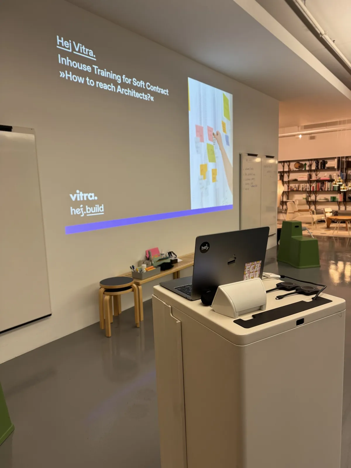 Vortragspult mit Laptop vor der Startfolie des Seminars »Inhouse Training for Soft Contract« mit den Logos von Vitra und hej.build