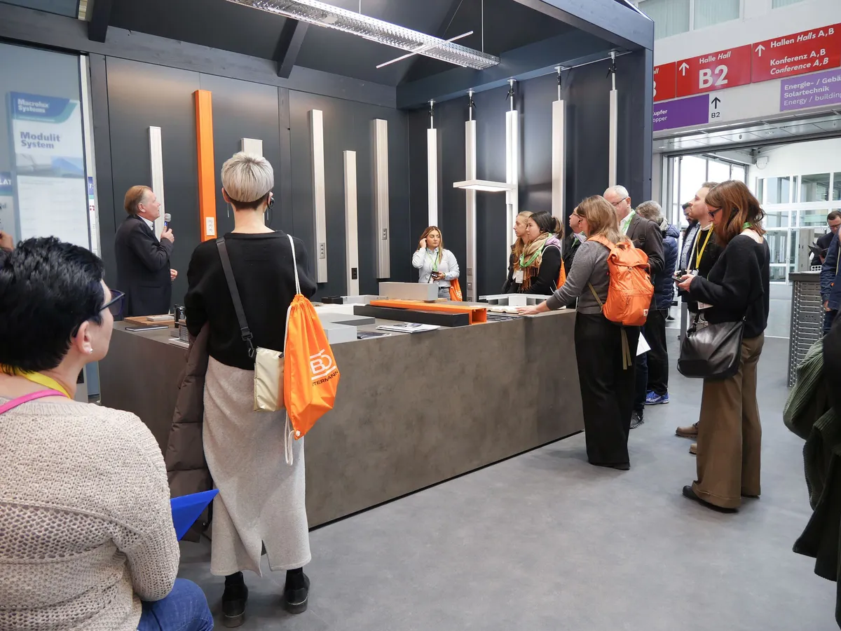 Führung am OBO Messestand: Gruppe mit orangefarbenen OBO-Beuteln vor einer Produktwand mit Installationssäulen