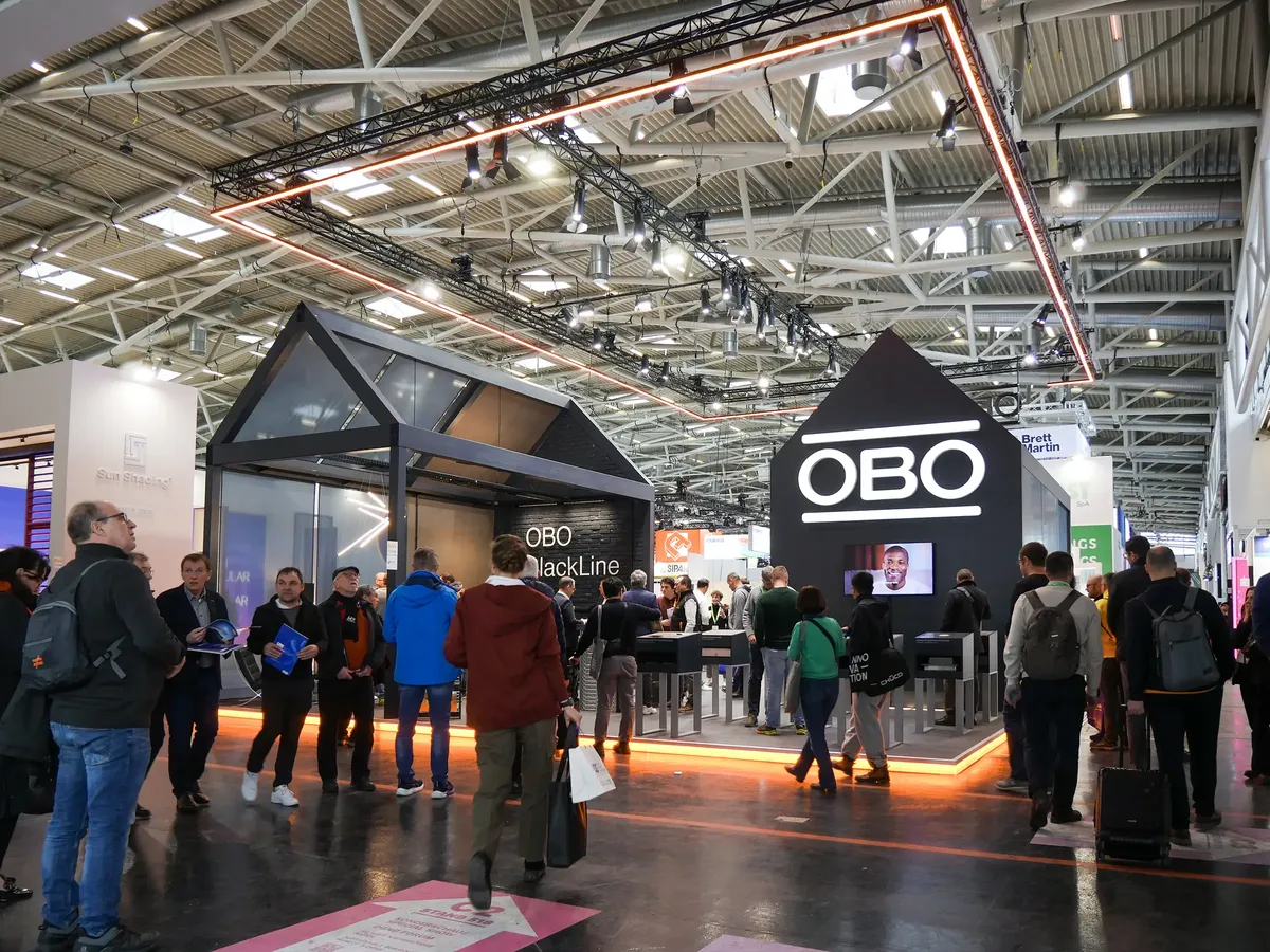OBO Bettermann Messestand auf der BAU 2025 mit zwei hausförmigen Pavillons, OBO-Logo und vielen Besucher:innen