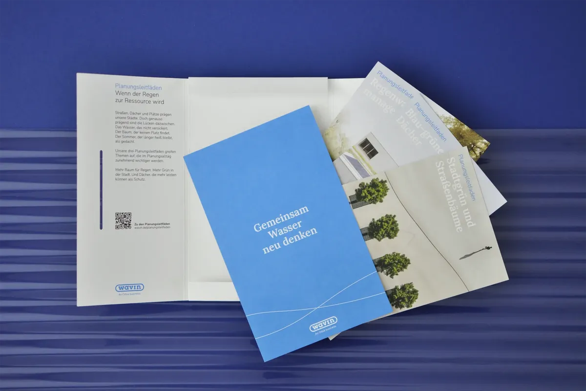 Geöffnete Mailing-Mappe von Wavin mit der Einlegekarte »Gemeinsam Wasser neu denken« und Planungsleitfäden auf blauem Untergrund