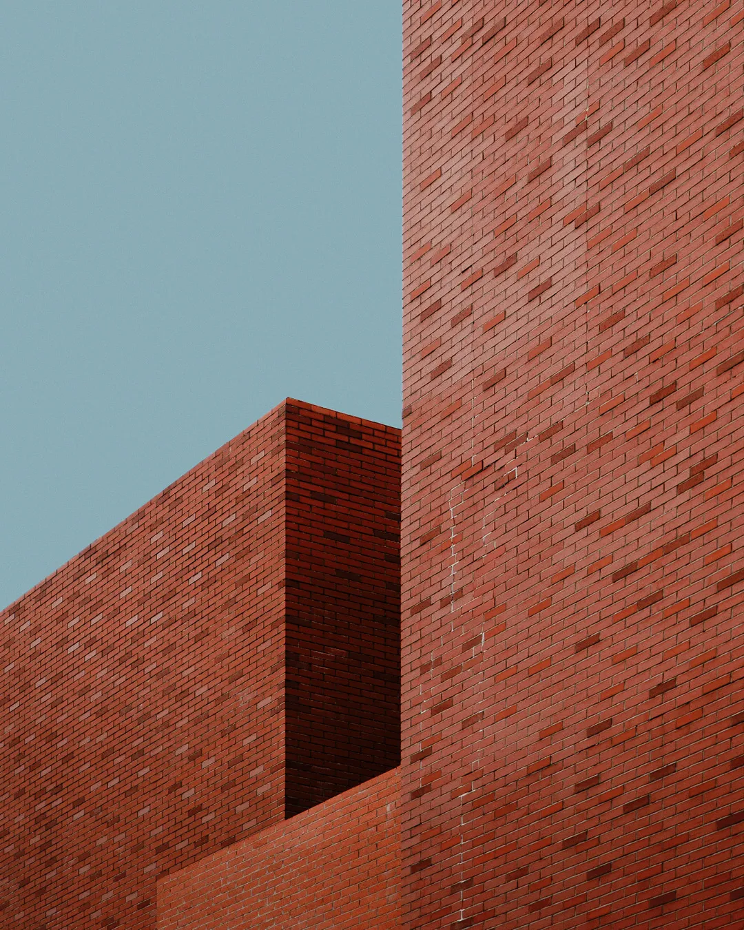 Rote Klinkerfassade mit zwei gegeneinander versetzten Mauerwerksscheiben vor blauem Himmel