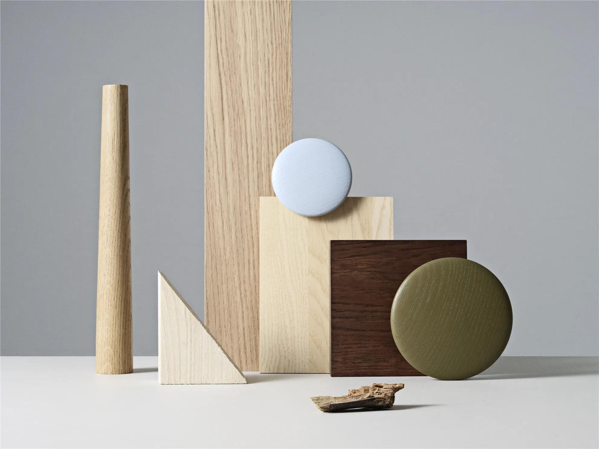 Stillleben mit Holzmustern, Farbflächen und geometrischen Formen in der Muuto-Farbwelt. Helle Hölzer, Olivgrün und Hellblau vor grauem Hintergrund.