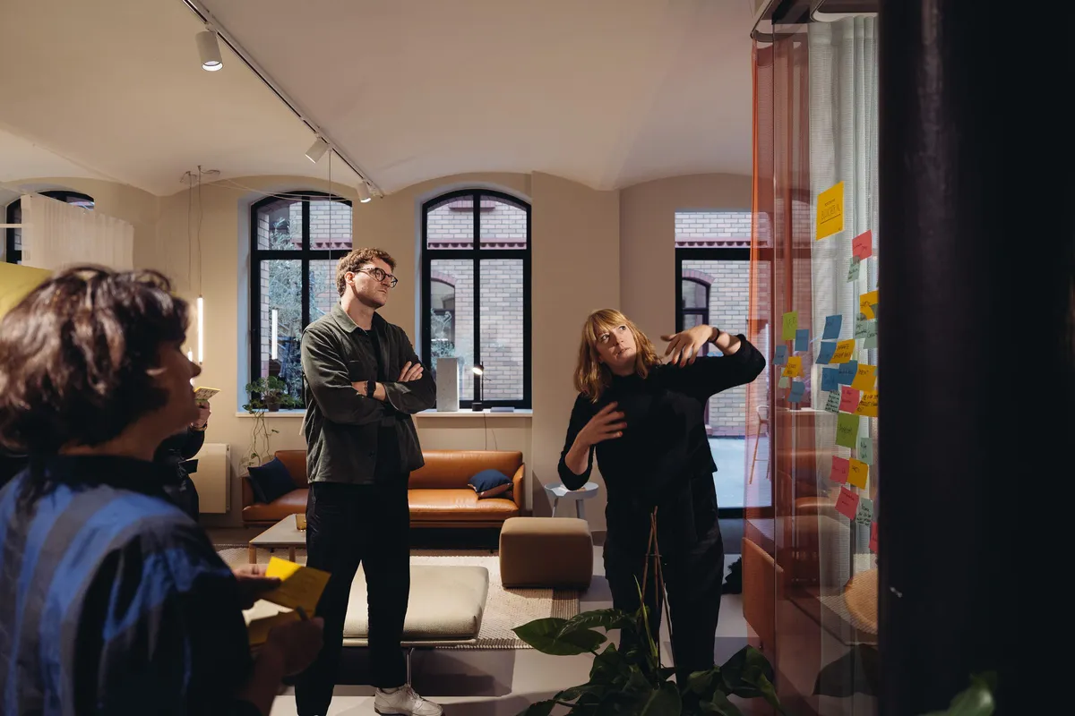 Workshop in einem Showroom: drei Personen vor einer Glaswand mit Haftnotizen, eine davon gestikuliert