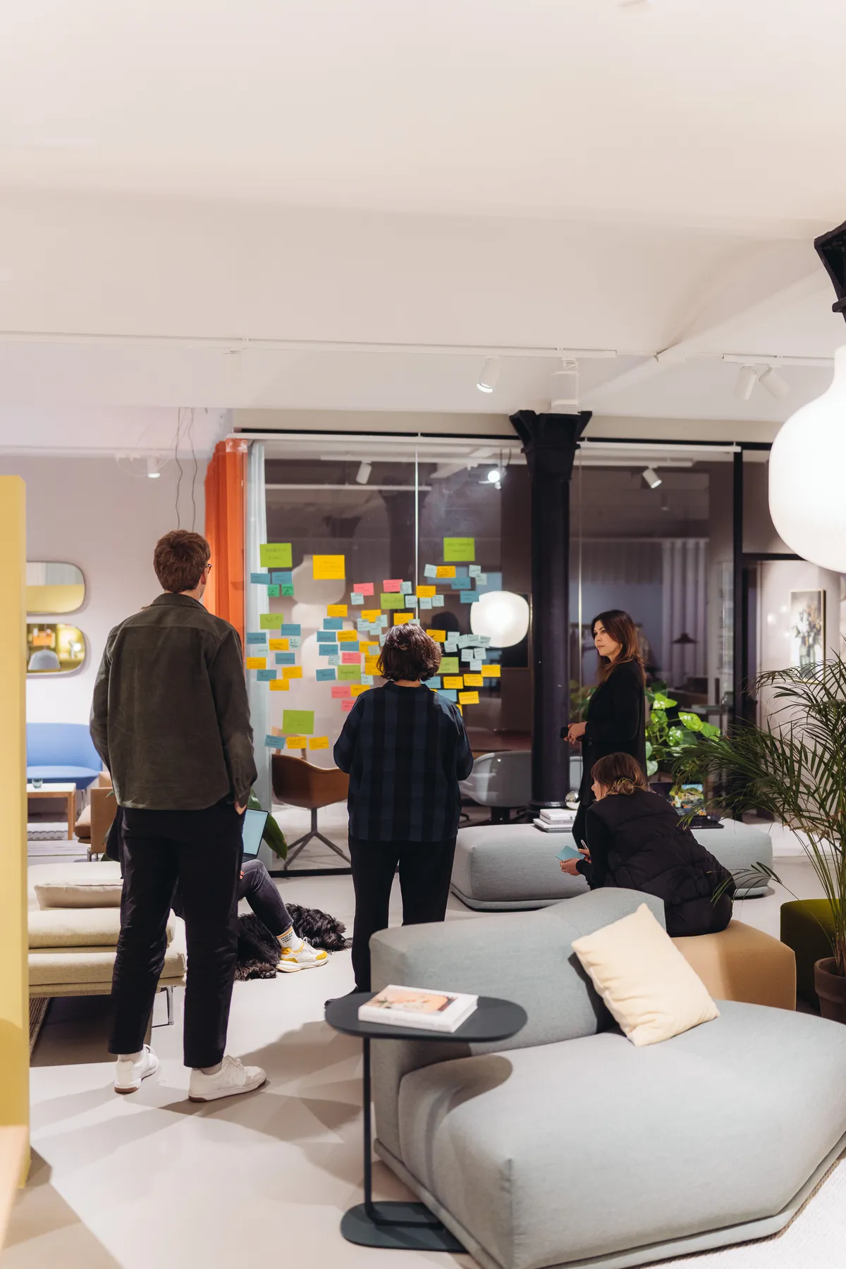 Teilnehmende arbeiten an einer Glaswand voller Haftnotizen in einem Showroom mit Sofas