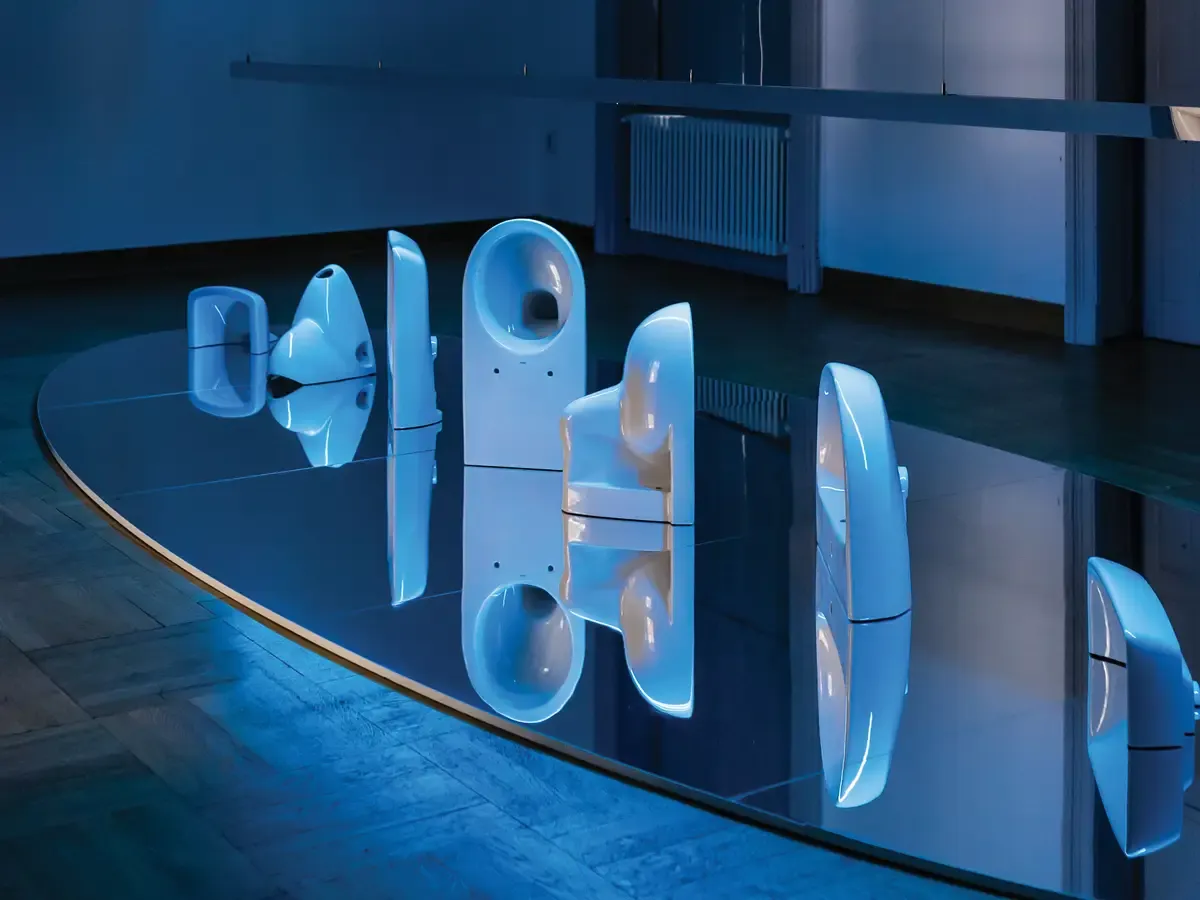Installation ROTA ET SPECULUM von Geberit, gestaltet vom hanczar studio: Sanitärkeramik auf einer großen Spiegelplatte, inszeniert in blauem Licht