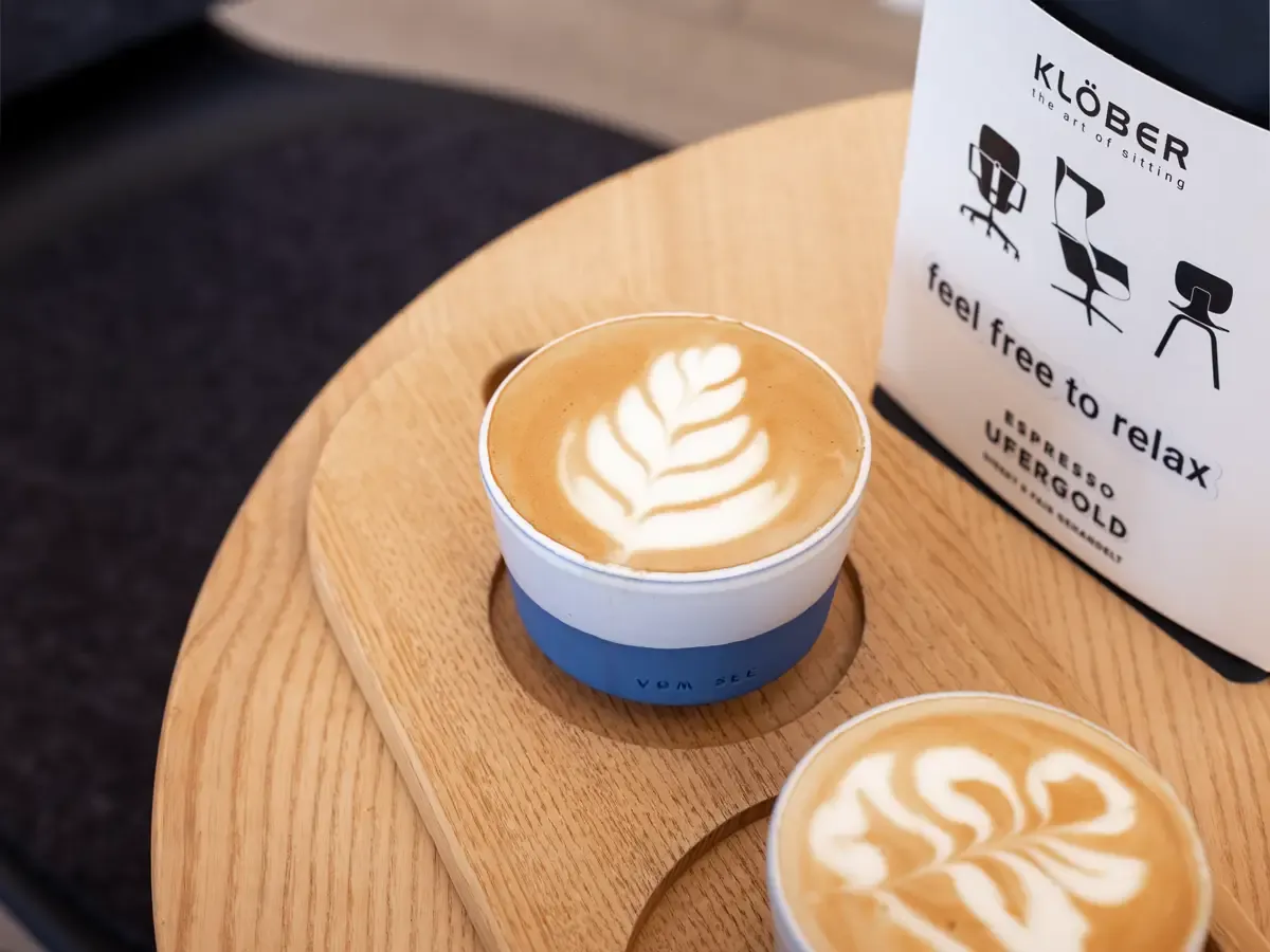 Zwei Cappuccinos mit Latte Art auf Holztisch neben einer Packung Klöber Espresso Ufergold