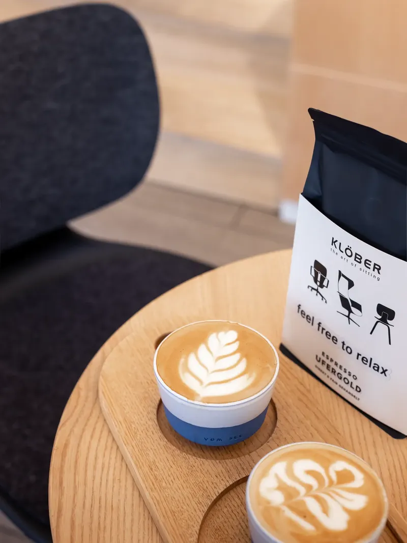 Zwei Cappuccinos mit Latte Art auf Holztisch neben einer Espressopackung von Klöber.