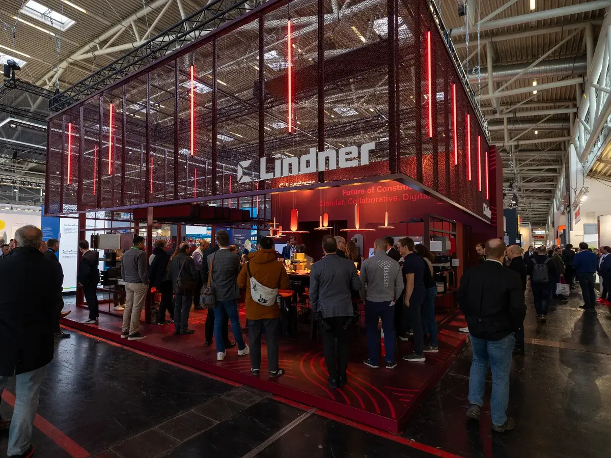 Lindner Group Messestand auf der BAU 2025: markante rote LED-Beleuchtung und Streckmetall-Architektur mit 'Future of Construction' Claim, gut besuchter Beratungsbereich