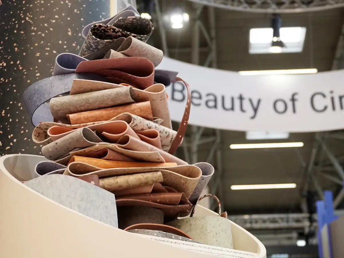 Kunstvoll drapierte Vinylbodenreste in Erdtönen, gestapelt vor einem 'Beauty of Cir'-Banner auf dem Tarkett Messestand der BAU 2025