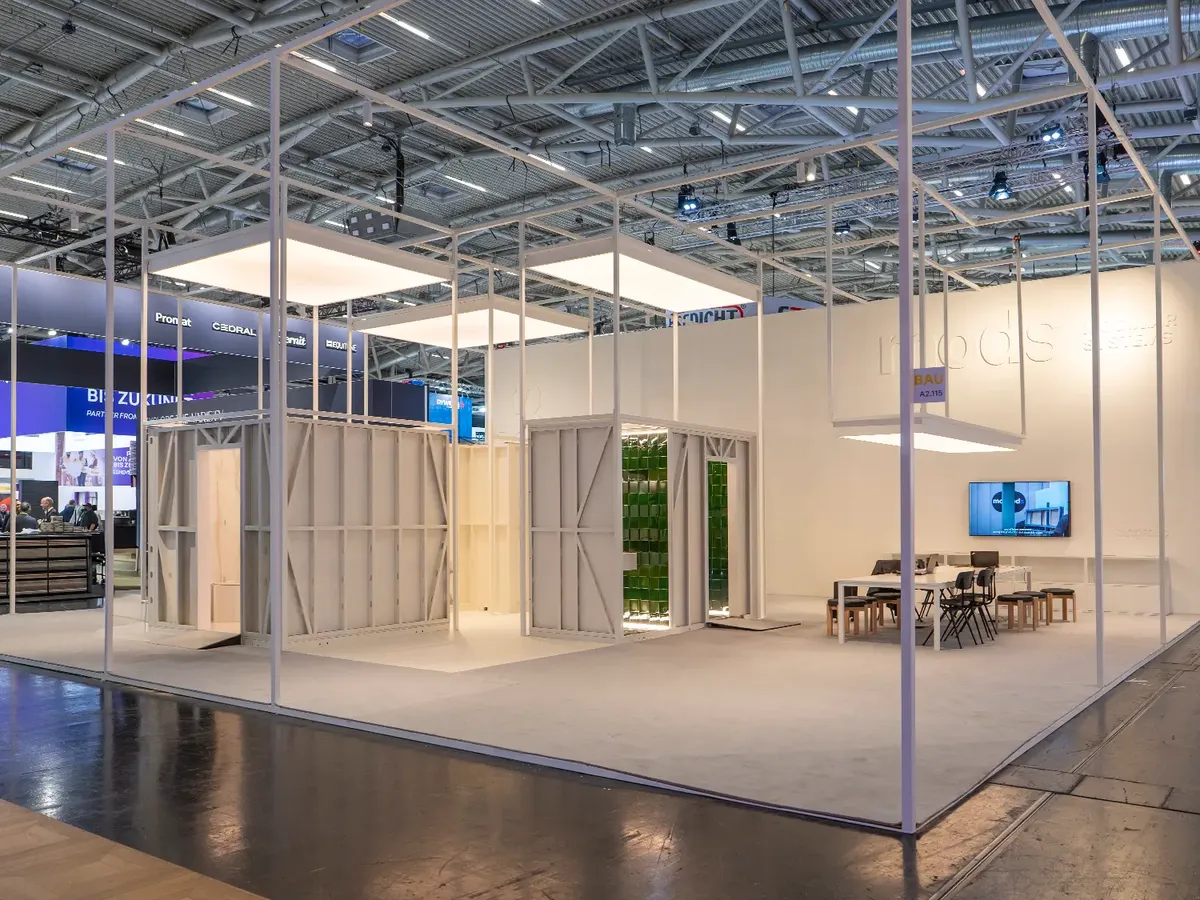 MODS Messestand mit modularen Sanitärboxen in Cremeweiß, kontrastiert mit portugiesischen Fliesen und laborähnlichen Lichtkästen