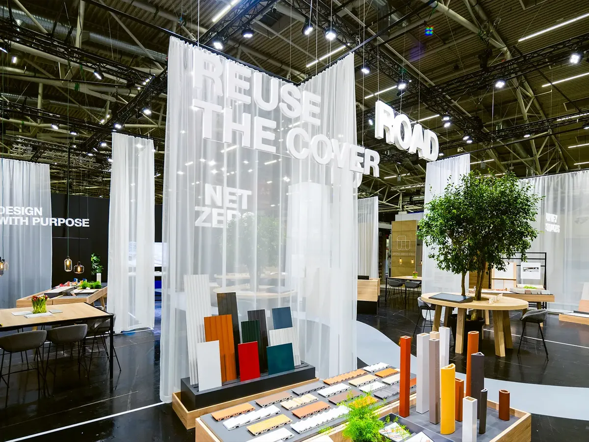 Messestand mit 'Reuse the Cover' Motto, weiße Vorhänge und Produktpräsentation in Erdtönen, ergänzt durch grüne Pflanzen und Beratungstische auf der BAU 2025