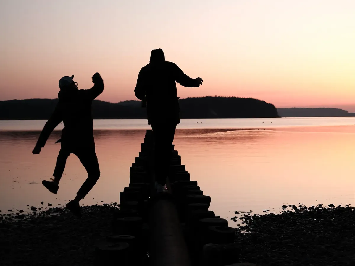 Silhouetten der hej.build Gründer Michael Rahmfeld und Hannes Eberlein bei Sonnenuntergang am Meer, einer springt: Symbol für Aufbruch, Vision und die Zukunft der Strategieberatung.