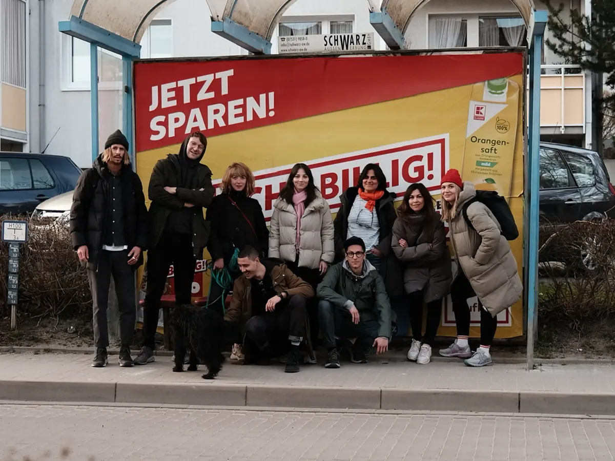 Das hej.build Team während der Workation 2022 auf Rügen, humorvoll posierend vor einem »JETZT SPAREN! BILLIG!«-Werbeplakat, eine Anspielung auf sich verändernde Marktbudgets und die Anpassungsfähigkeit der Strategieberatung.