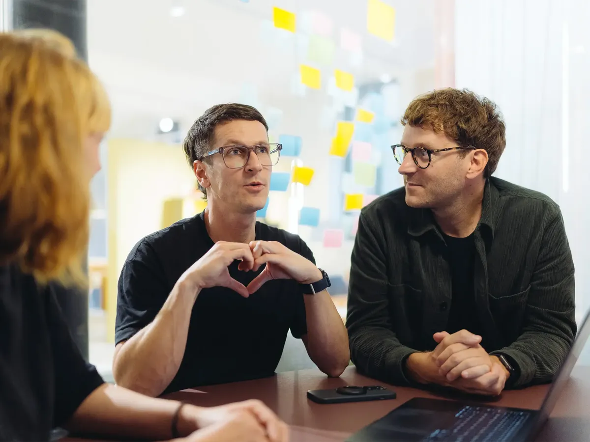 hej.build Gründer Michael Rahmfeld (Sales-Fuchs) formt ein Herz mit den Händen um Co-Gründer Hannes Eberlein (Tech-Schwein), Ausdruck ihrer starken Partnerschaft und der wertschätzenden Unternehmenskultur.