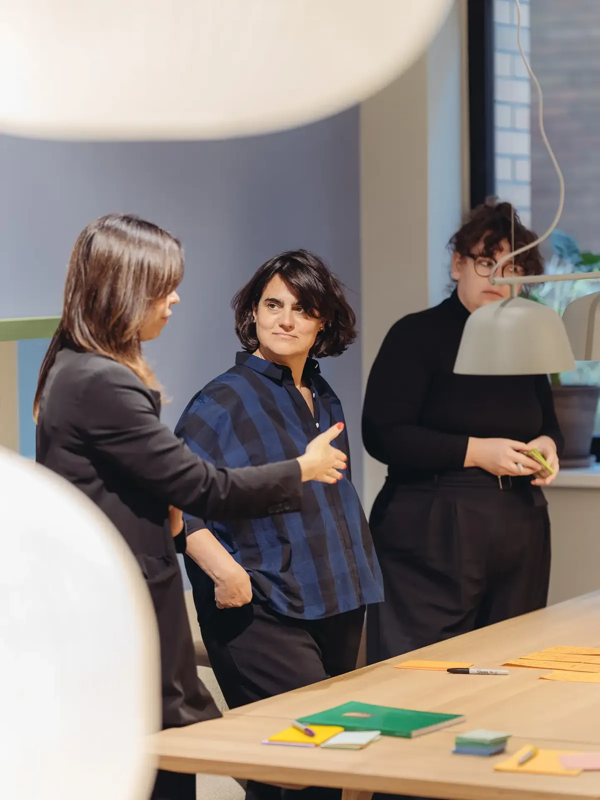 Drei Architektinnen und Designerinnen in einer kreativen Workshop-Situation, diskutieren Konzepte am Tisch.