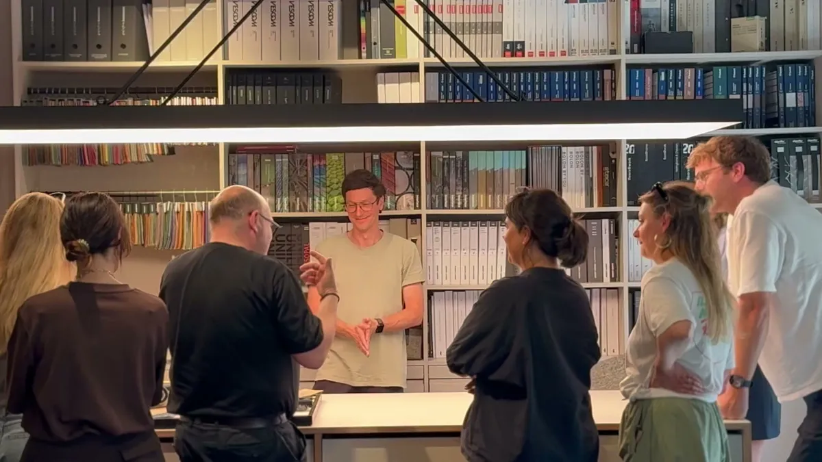 A group standing in a material library with shelves full of sample folders, listening to one person