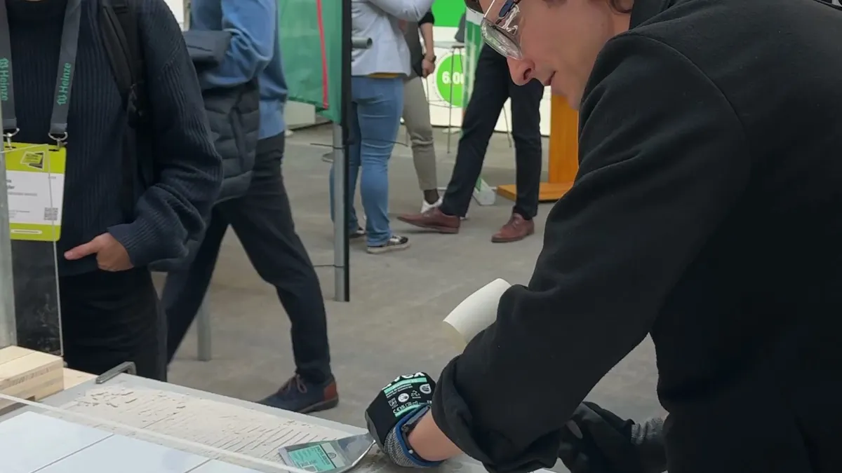 A man in safety glasses and a work glove removing tiles at the deconstruction station while visitors watch