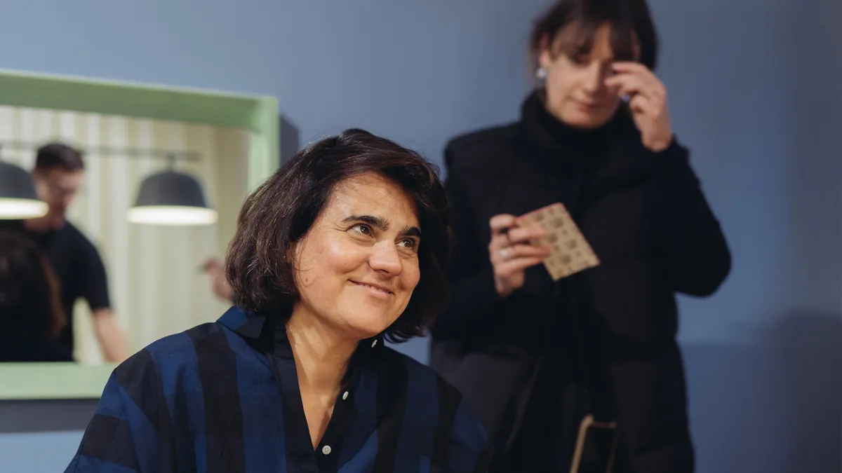 A woman with dark hair smiling during the workshop, behind her a second woman looking at a small sample