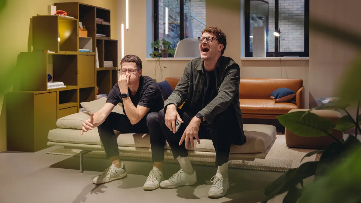 Two men laughing on a sofa in a showroom with shelves