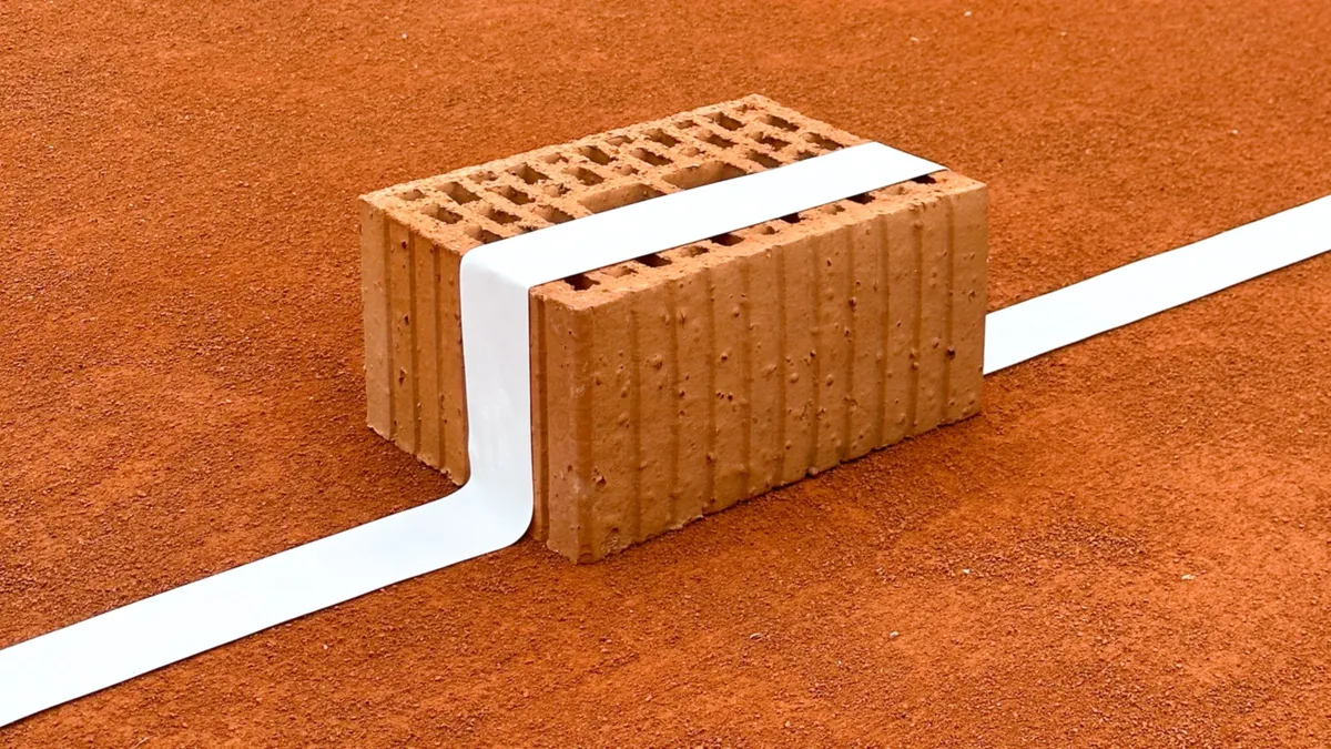 A brick on a red clay court with a white line running over it: a staged product photo for wienerberger