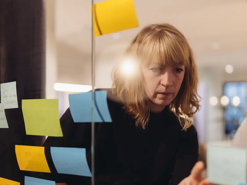 A person arranging colourful sticky notes on a glass wall
