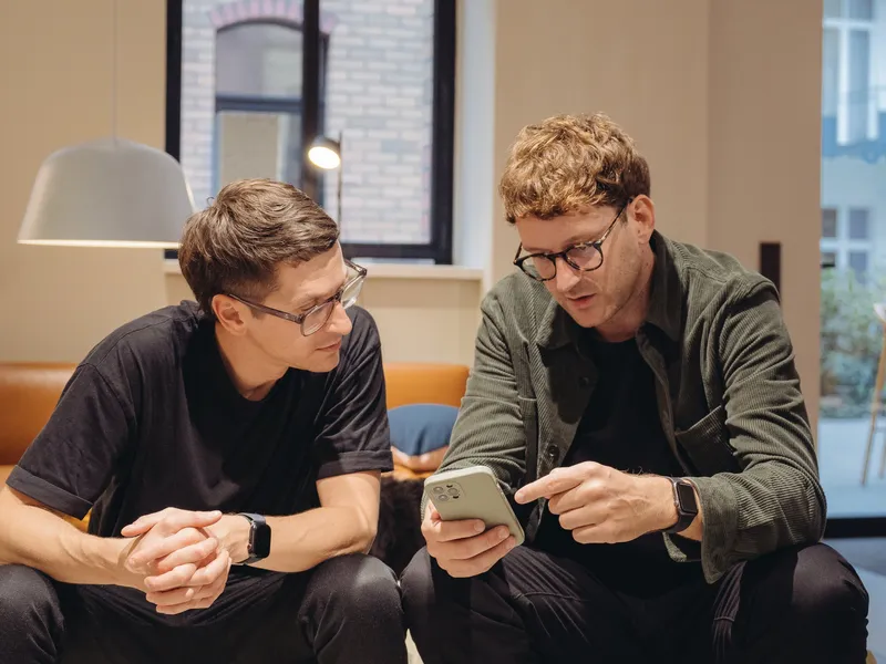 Two men on a sofa in a showroom, one showing the other something on his phone