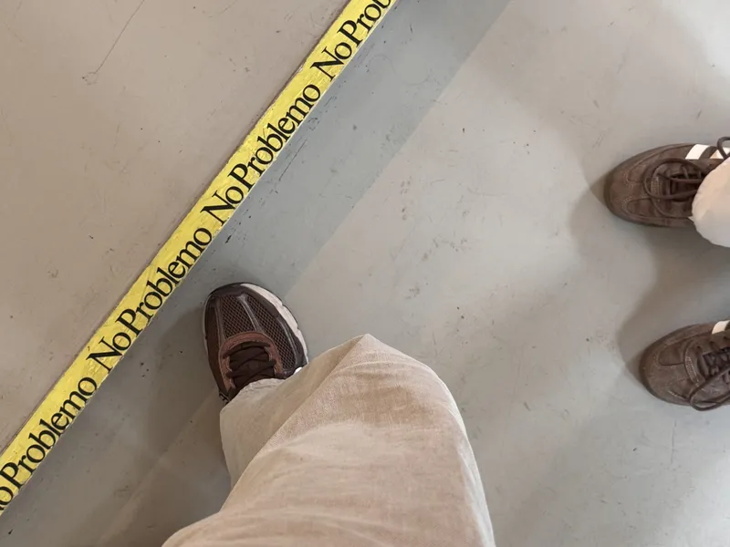 View from above of shoes and a yellow tape printed with »No Problemo« on a grey floor