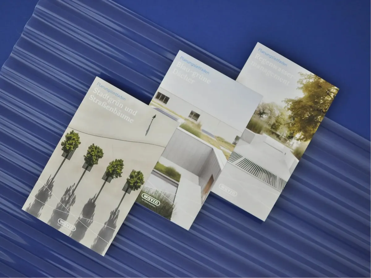 Drei Broschüren mit Architekturfotos auf blauem Trapezblech