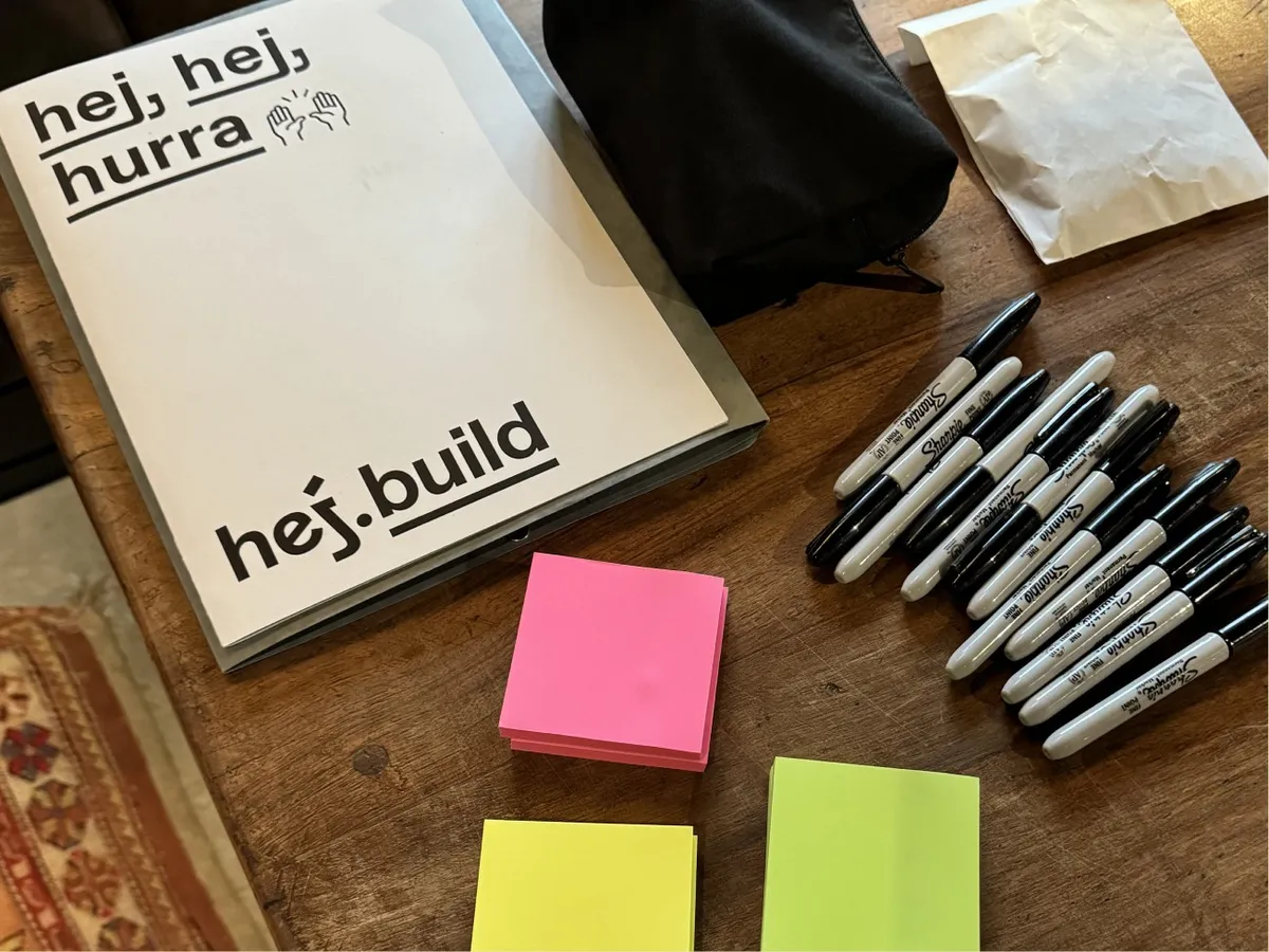 Workshopmappe »hej, hej, hurra« von hej.build mit Markern und Haftnotizen auf einem Holztisch