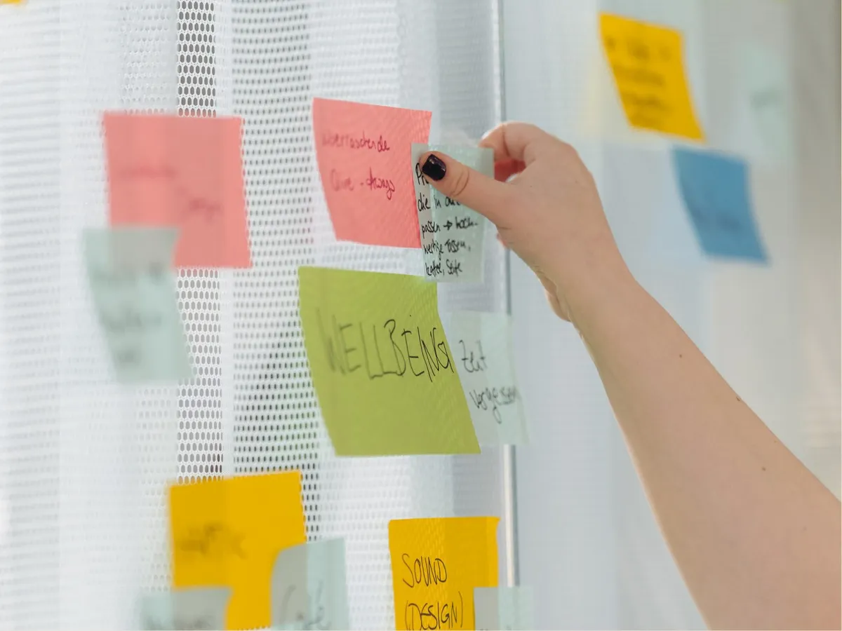Hand klebt beschriftete Haftnotizen an eine helle Wand